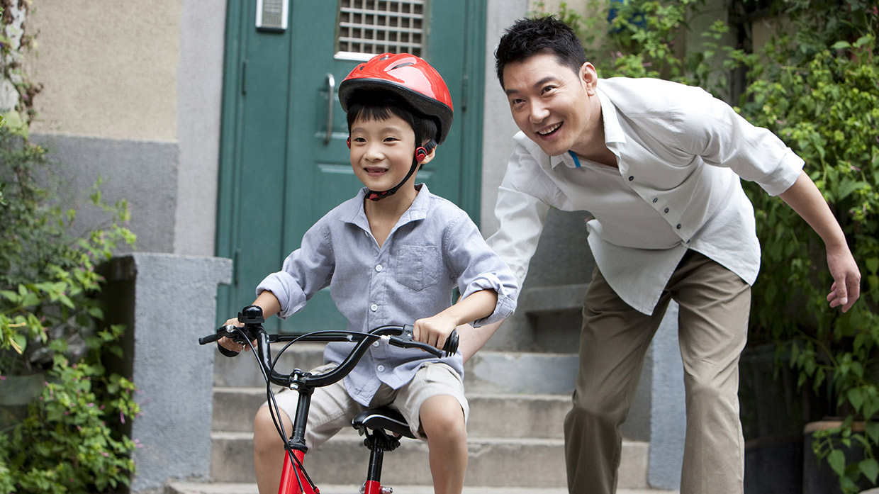 A father is teaching his son to ride a bicycle, image used for HSBC Malaysia Amanah protection page.