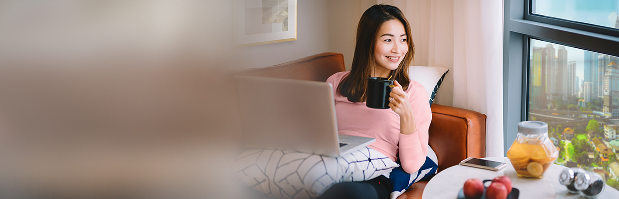A women is using laptop and drinking coffee in the living room; image used for HSBC Malaysia Amanah Auto Balance Conversion page.