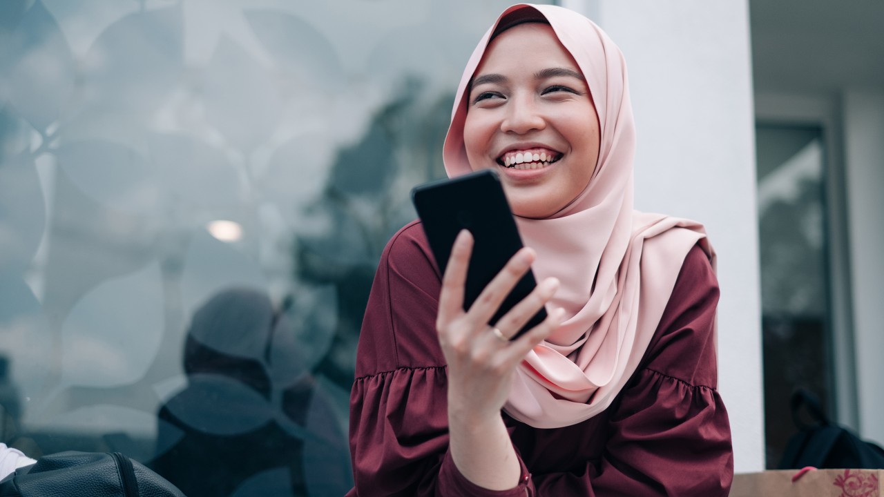 A smiling woman holding a phone; image used for HSBC Malaysia Amanah Mobile Banking