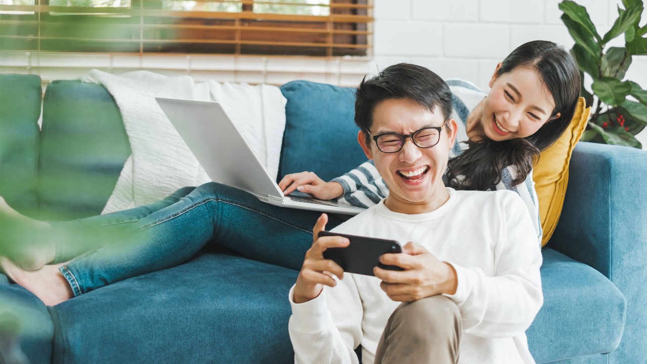 A man is using mobile with his girlfriend using laptop next to him; image used for HSBC Malaysia 6 ways personal financing can change your life article page.