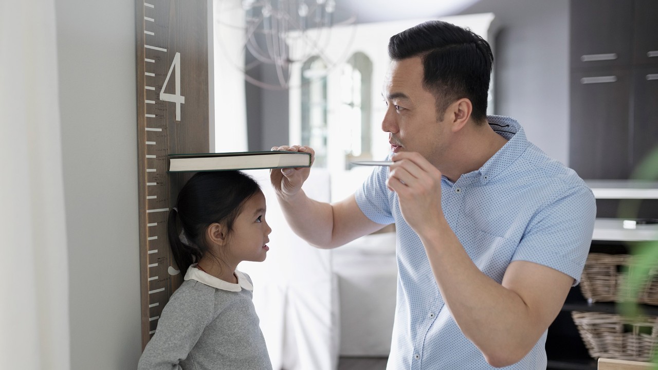 A father measuring his daughter’s height against a wall; image used for HSBC basic savings/current account-i page.