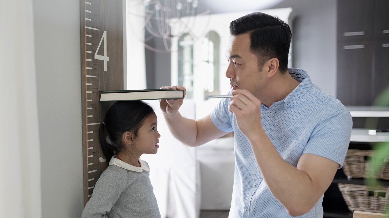 A dad is measuring the height of his daughter; imaged used for HSBC Malaysia Amanah Basic Savings/ Current Account-i page.