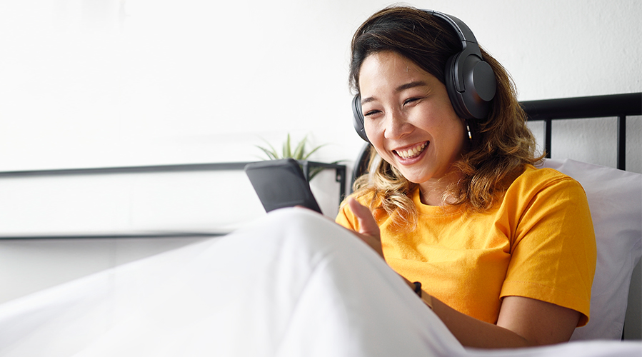 A woman is using a phone in bed; image used on HSBC Malaysia benefits of online banking article page.