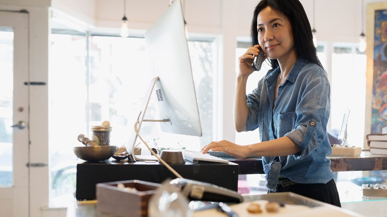 A woman is using a computer and talking on the phone; image used for HSBC Malaysia Amanah telebanking