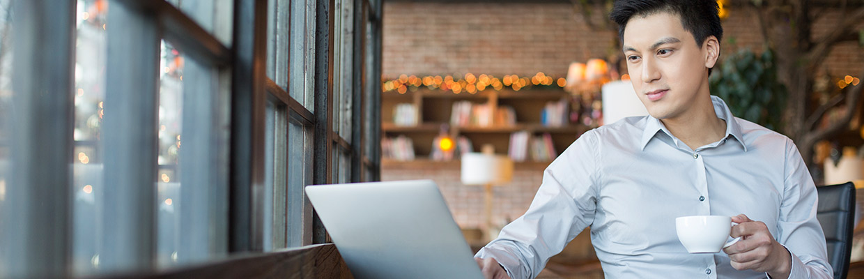 A man is holding a cup while looking at the laptop; imaged used for HSBC Malaysia Amanah Term Deposit-i page.