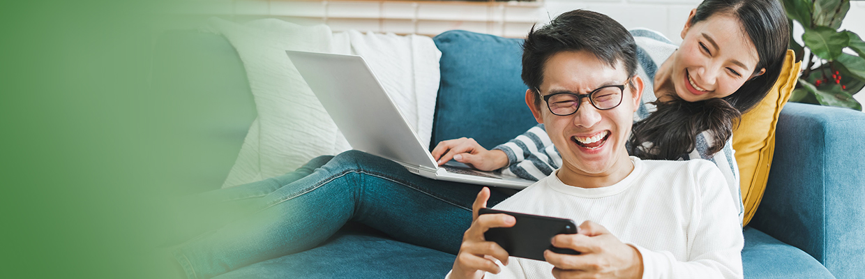 A man is using mobile with his girlfriend using laptop next to him; image used for HSBC Malaysia 6 ways personal financing can change your life article page.