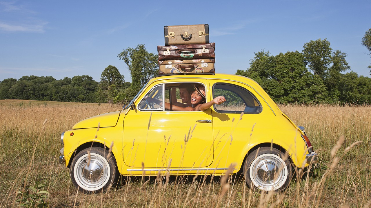 A woman driving a yellow car with suitcases on top; image used for HSBC faster access, more control page.
