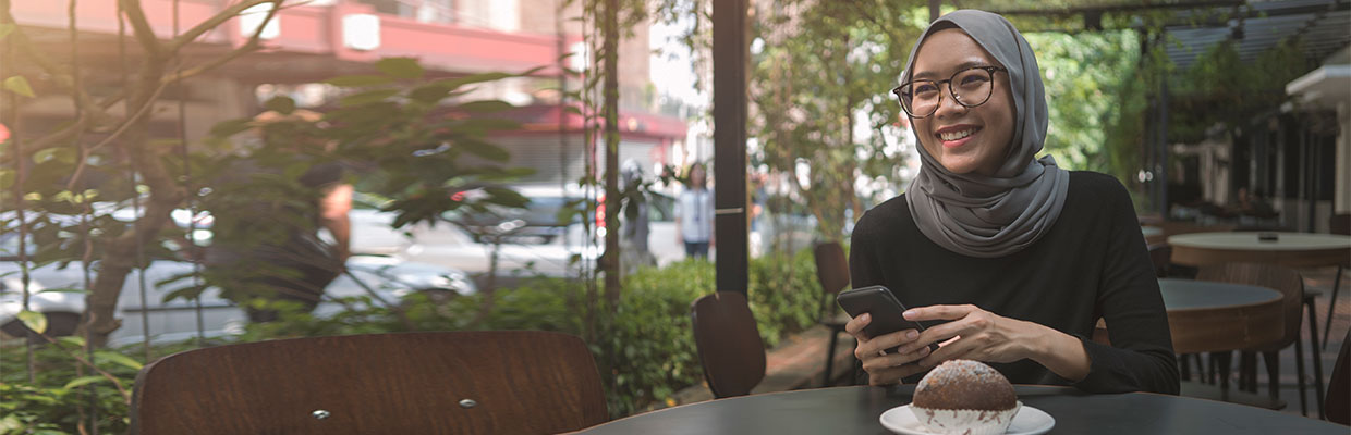 A young woman is happily sitting in a cafe, surrounding with lots of plants; imaged used for HSBC Malaysia Amanah financing concept 101 page. 