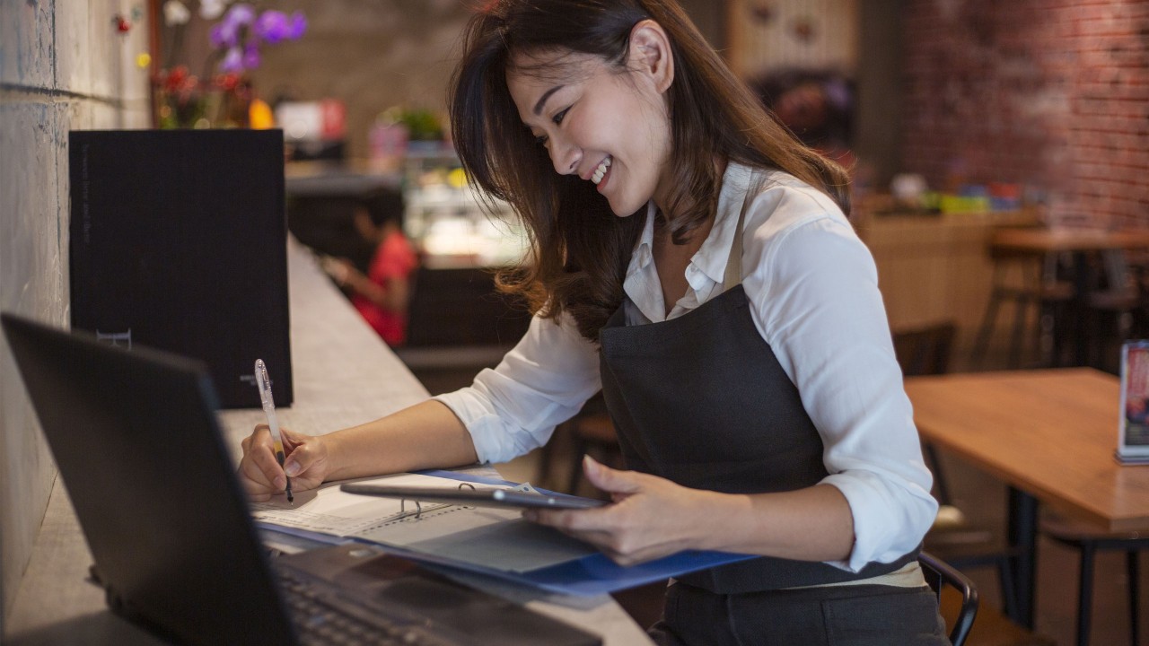 A woman is calculating financial report with a tablet and a laptop; image used for HSBC Amanah Fusion 'How can businesses adapt and bounce back' article page.