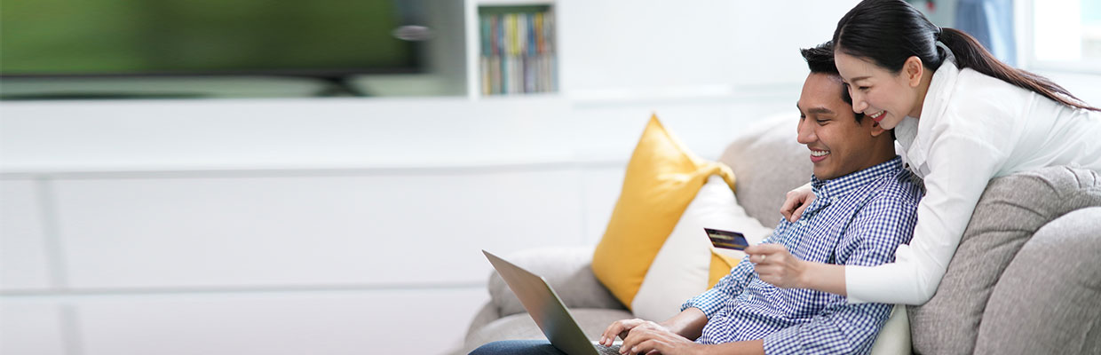 A happy couple is inputting credit card information into the laptop; image used for HSBC Amanah Balance Transfer page.